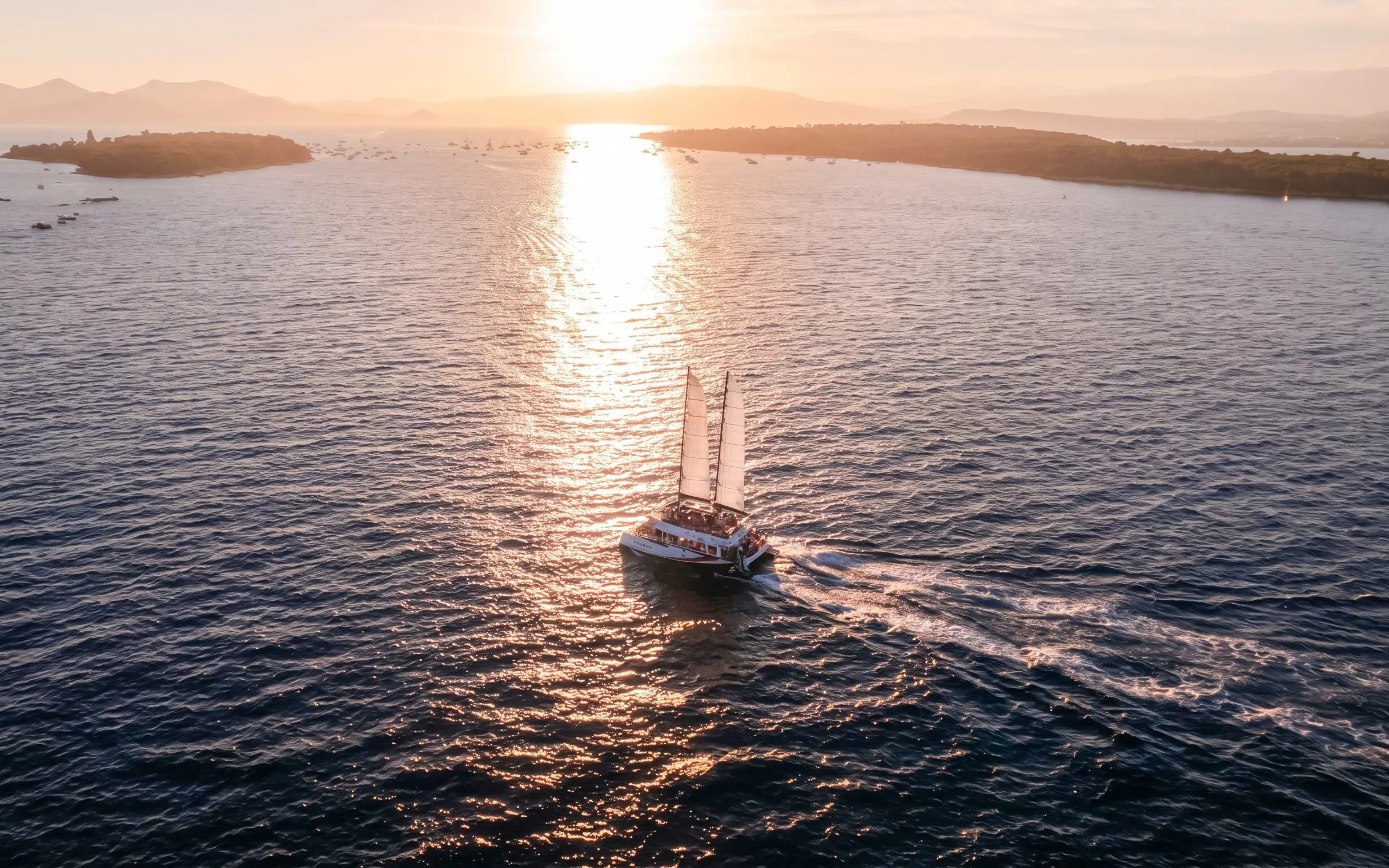Sailboat cruising at sunset on the French Riviera with distant coastline.