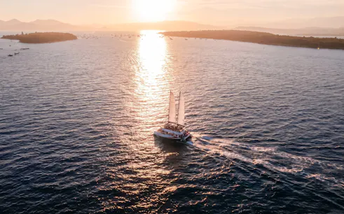 Sailboat cruising at sunset on the French Riviera with distant coastline.