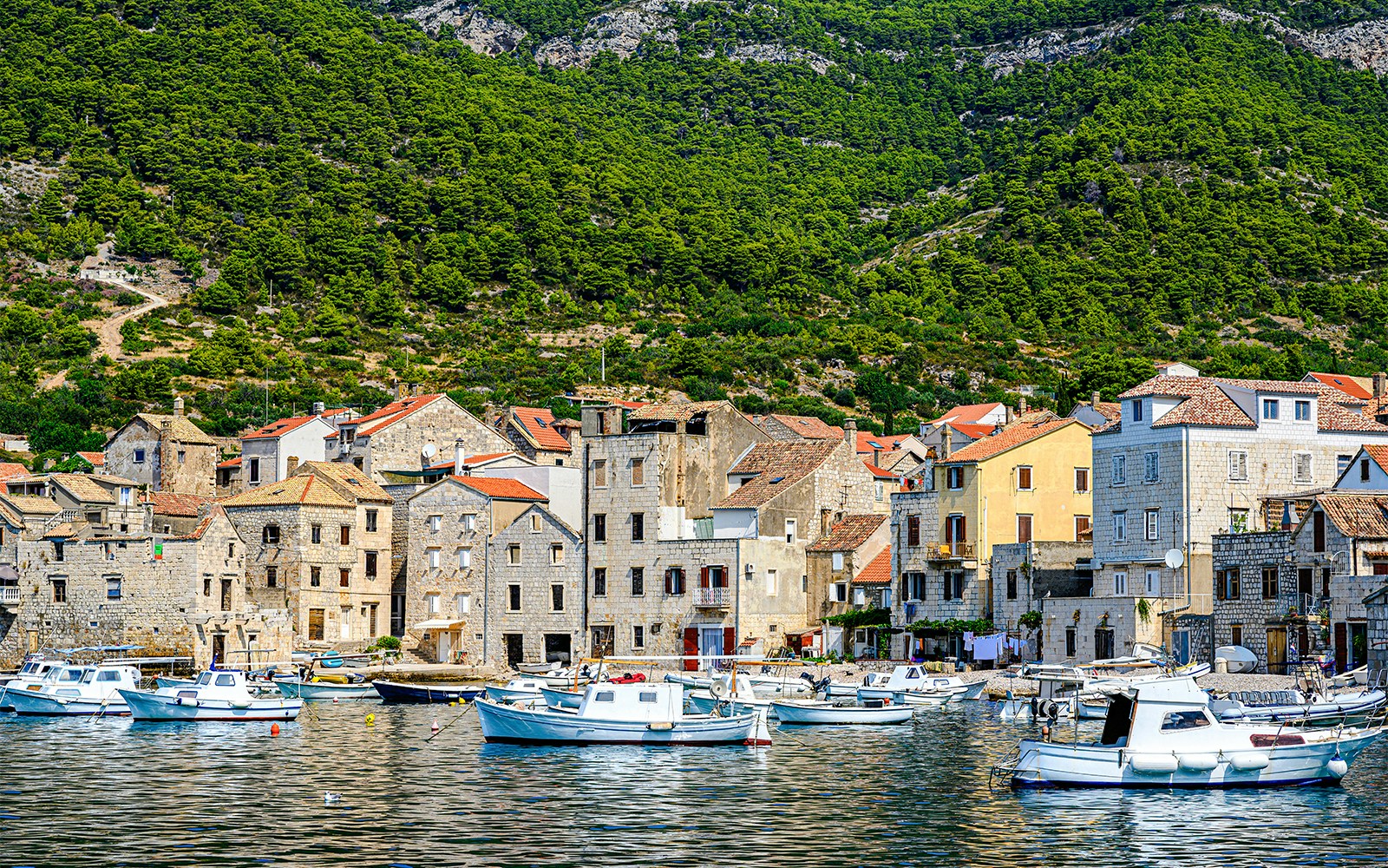 Boats docked along the waterfront of Komiža town, Vis island, Croatia, with hillside backdrop.