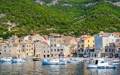 Boats docked along the waterfront of Komiža town, Vis island, Croatia, with hillside backdrop.