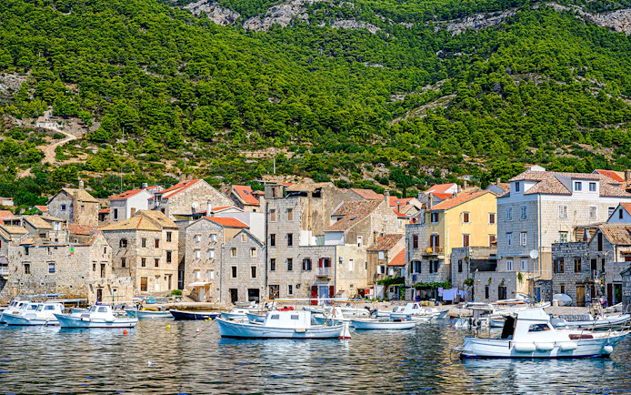 Boats docked along the waterfront of Komiža town, Vis island, Croatia, with hillside backdrop.