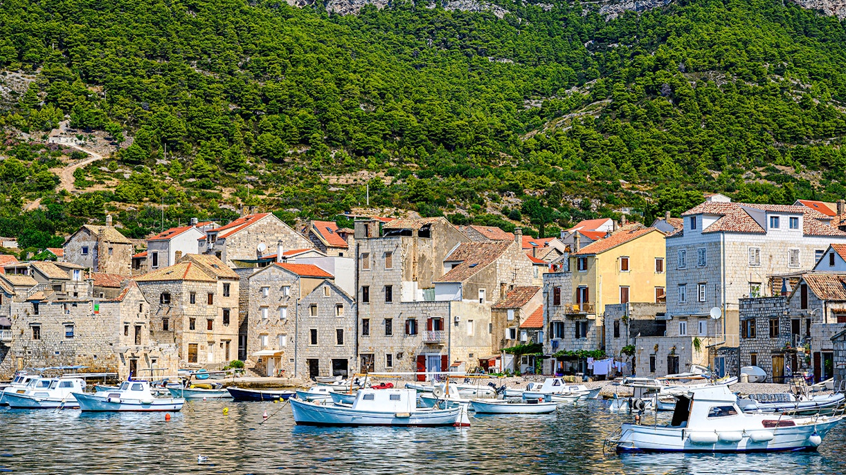 Boats docked along the waterfront of Komiža town, Vis island, Croatia, with hillside backdrop.