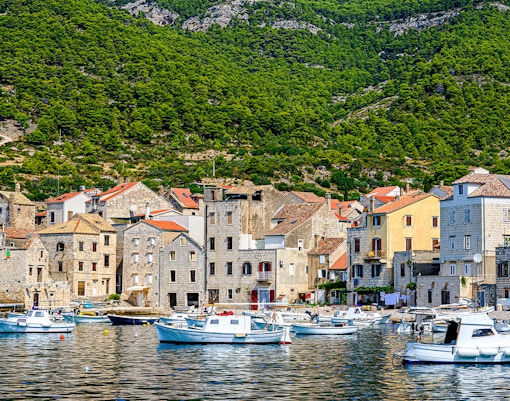 Boats docked along the waterfront of Komiža town, Vis island, Croatia, with hillside backdrop.