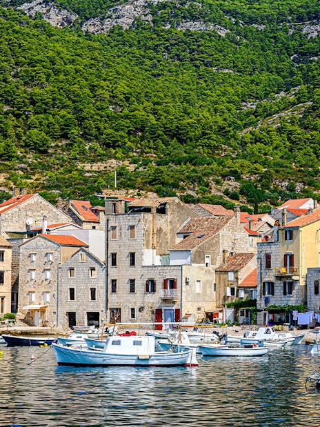 Boats docked along the waterfront of Komiža town, Vis island, Croatia, with hillside backdrop.