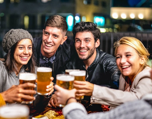 Group of friends toasting with beer glasses during a 3-hour beer tour in a lively setting.
