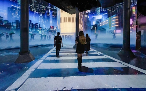 Guests walking through digital cityscape exhibit at ARTECHOUSE New York.