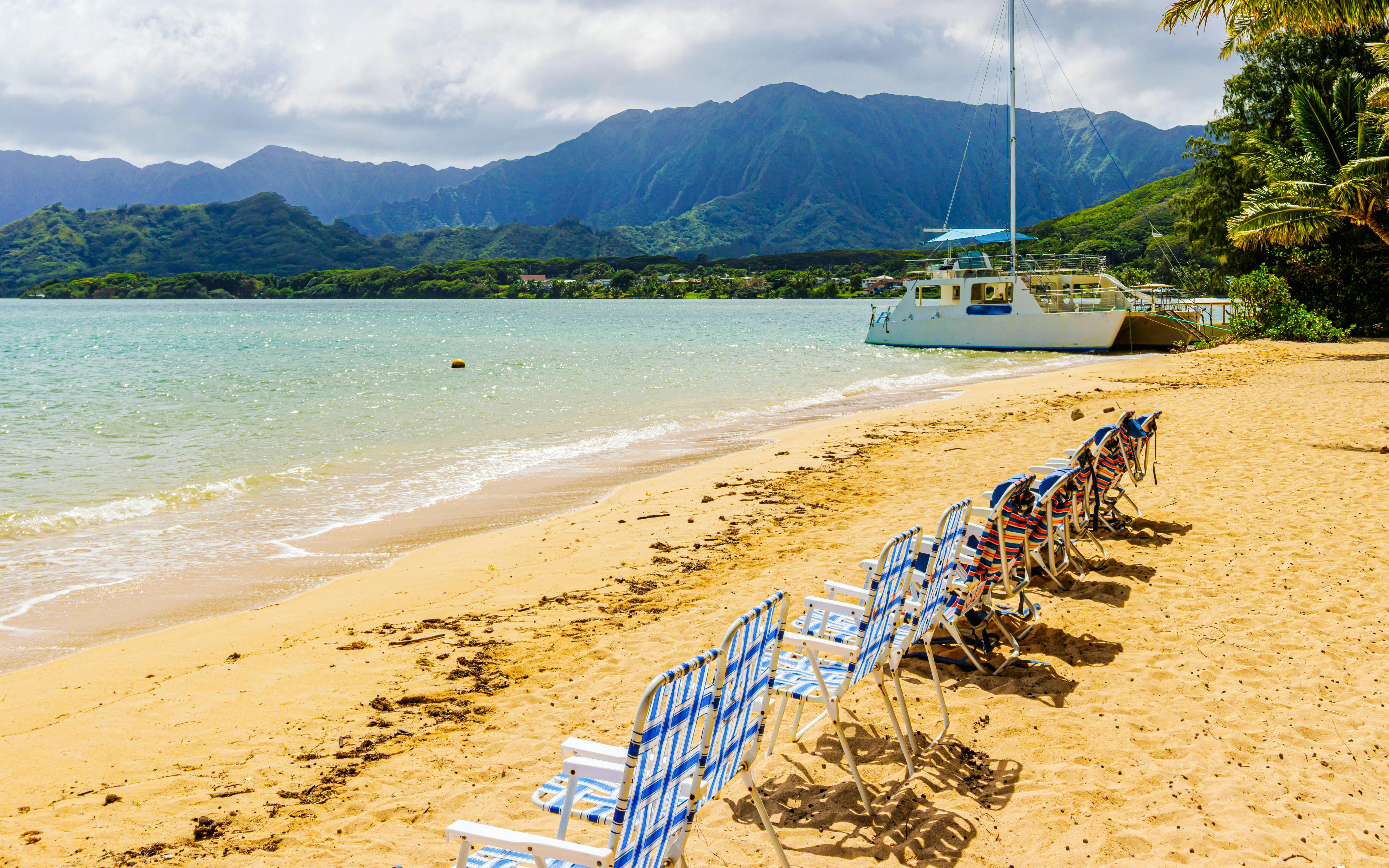 Chairs on sandy beach with boat in Kaneohe Bay, Kualoa Ranch, Hawaii.