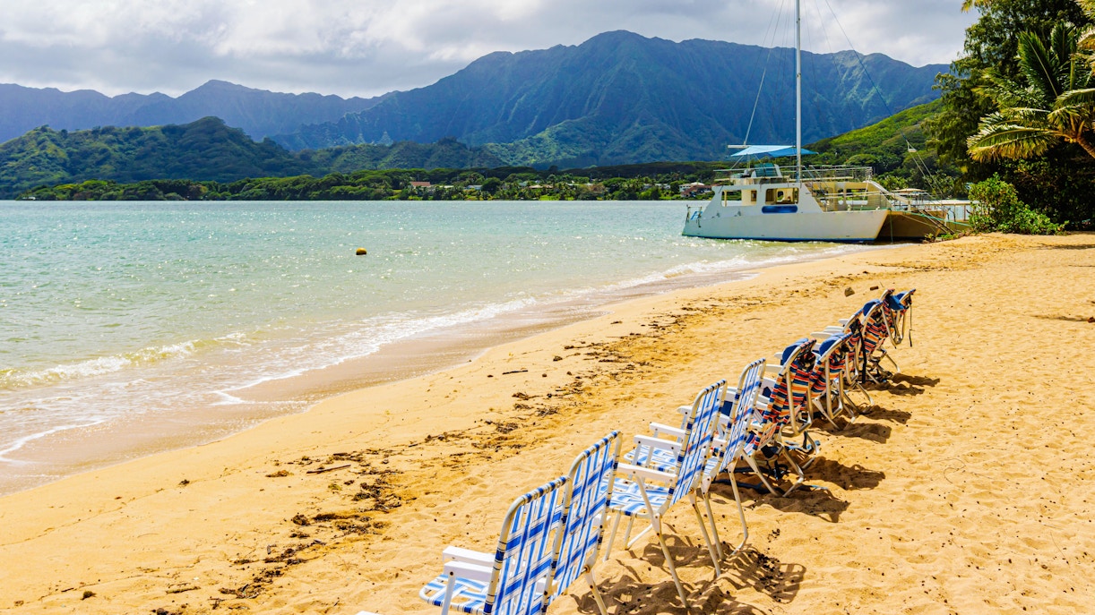 Chairs on sandy beach with boat in Kaneohe Bay, Kualoa Ranch, Hawaii.