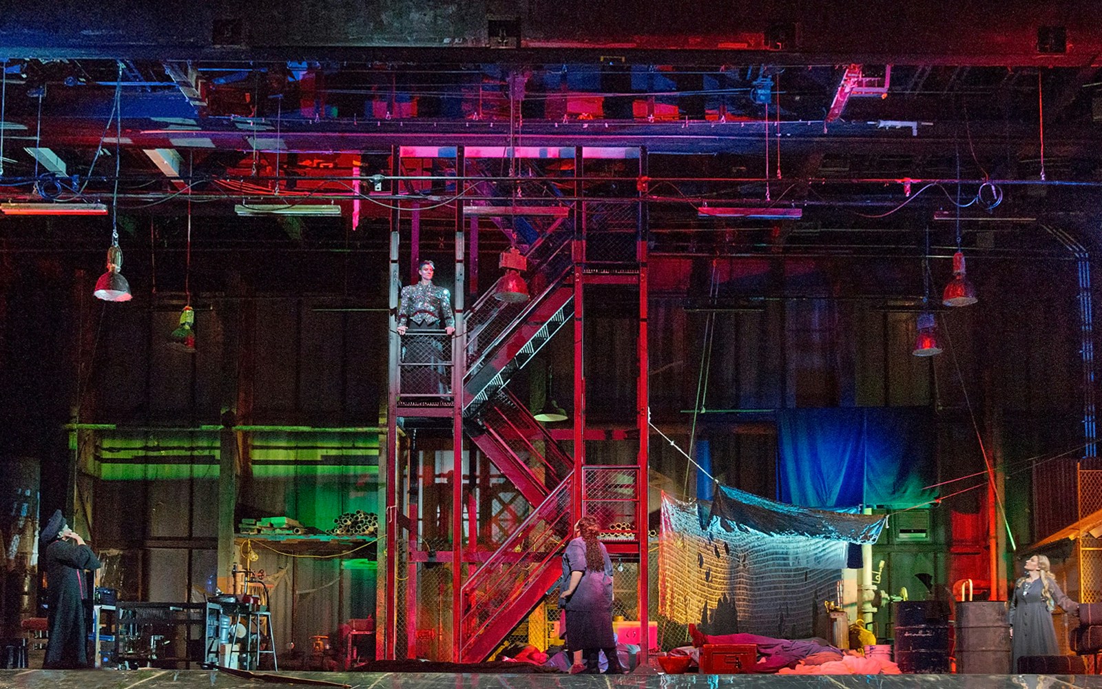 Stage set of "Die Frau Ohne Schatten" with colorful lighting and actors on a metal staircase.
