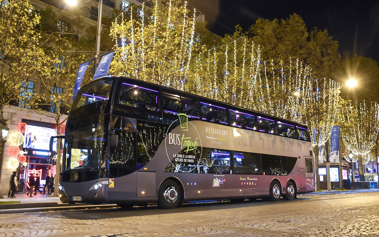 Bus Toqué Paris at night with festive lights on the Champs-Élysées.