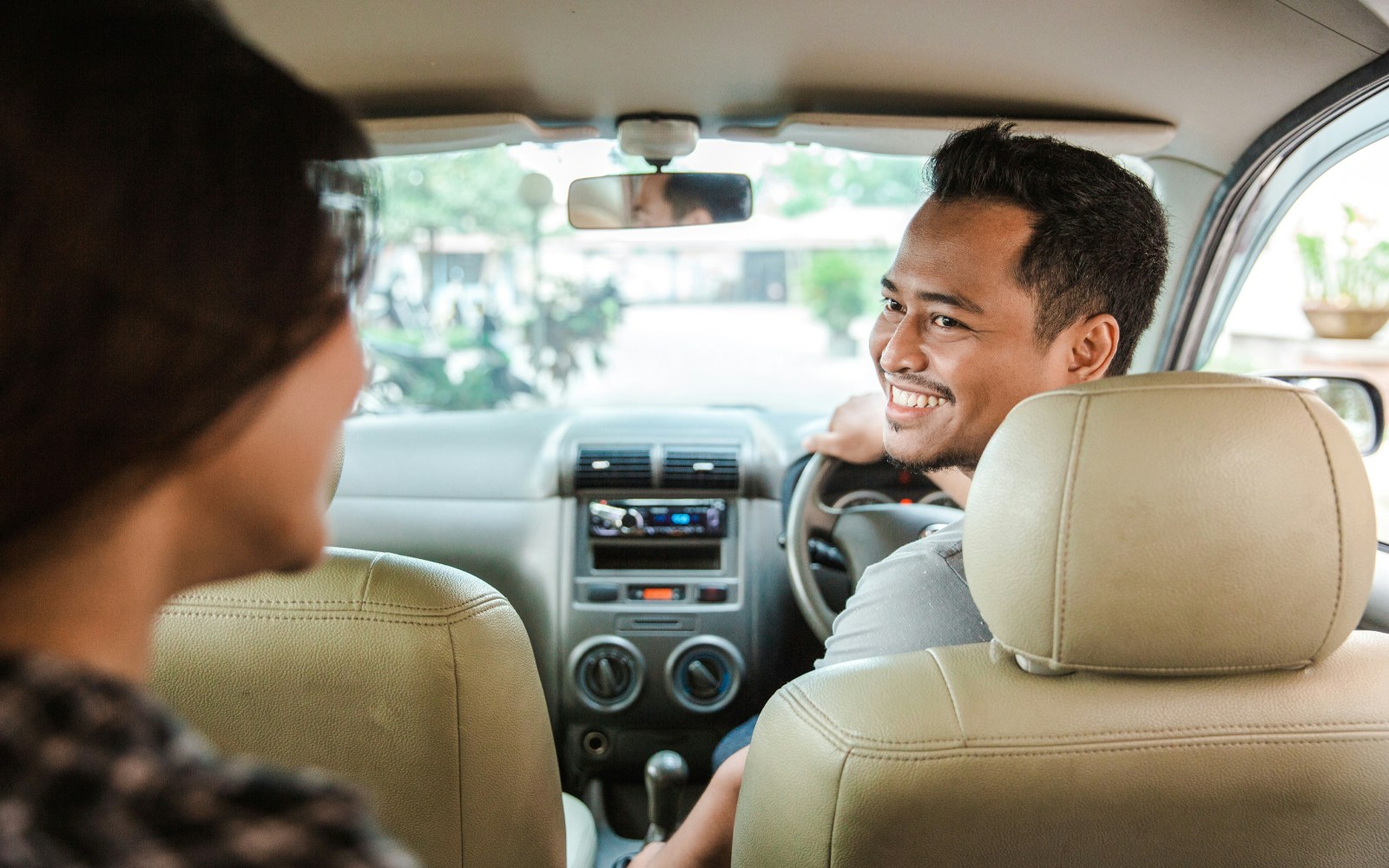 Person smiling while driving a taxi with a passenger in the back seat.