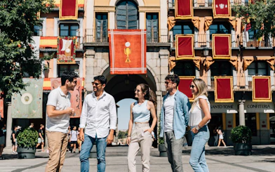 Tourists with guide at Corpus Christi procession in Toledo, Spain, standing in front of decorated building.