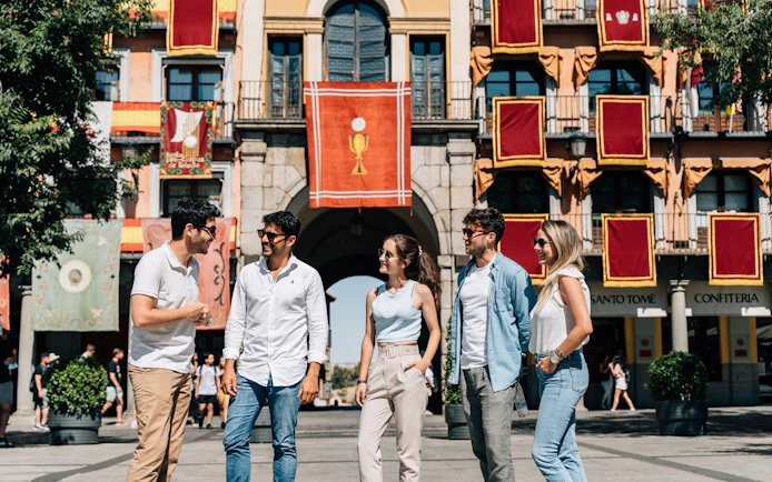 Tourists with guide at Corpus Christi procession in Toledo, Spain, standing in front of decorated building.