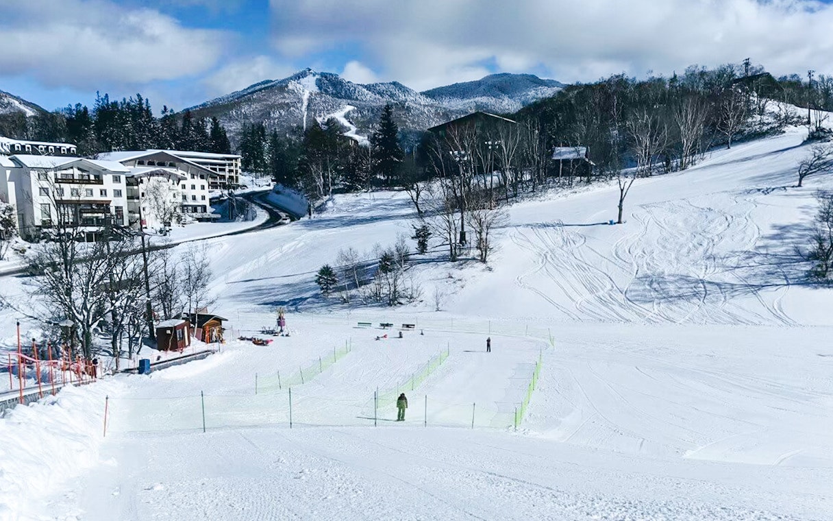 Snow-covered landscape with ski tracks and buildings in Nagano, Japan.