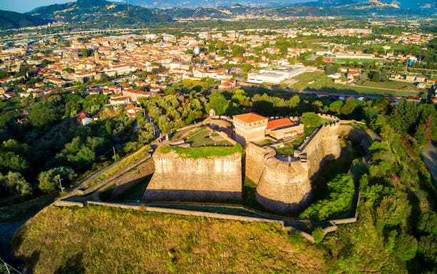 Aerial view of Fortezza di Sarzanello surrounded by lush greenery in Sarzana, Italy.