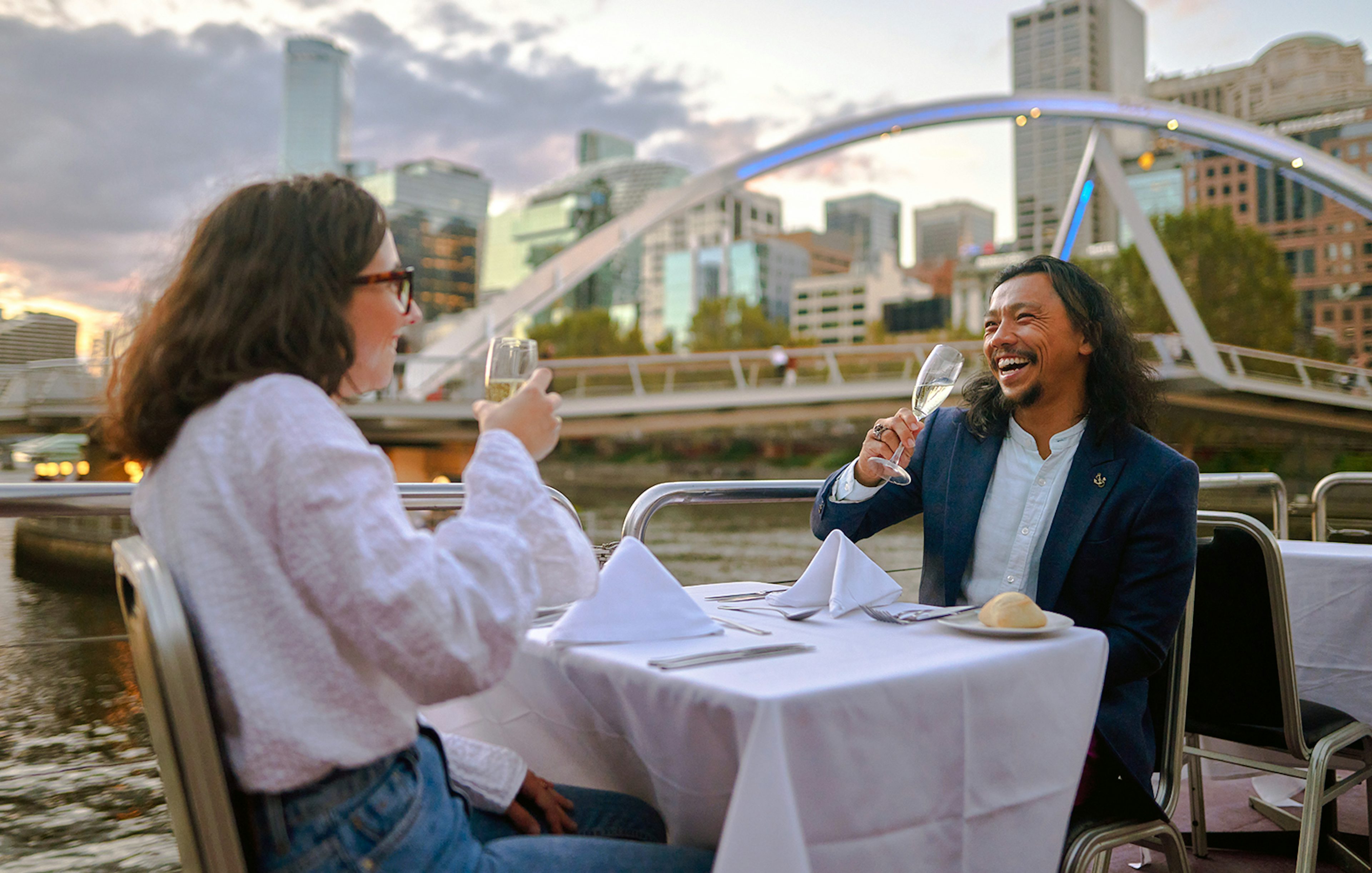 Couple enjoying wine on the Spirit of Melbourne Dinner Cruise with city skyline in the background.