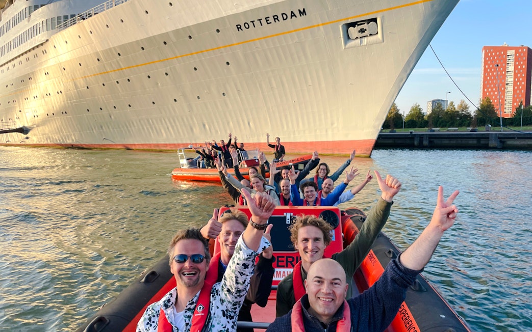 Group enjoying Rotterdam Harbour tour on RIB speedboat near large ship.