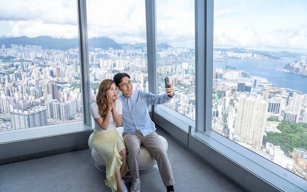 Couple taking a selfie at Sky100 Observation Deck with Hong Kong skyline in the background.