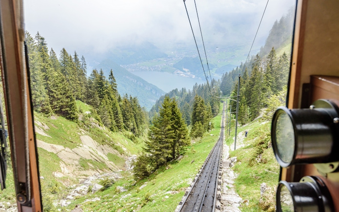 Mount Pilatus cogwheel train ascending through Swiss Alps with lake view.