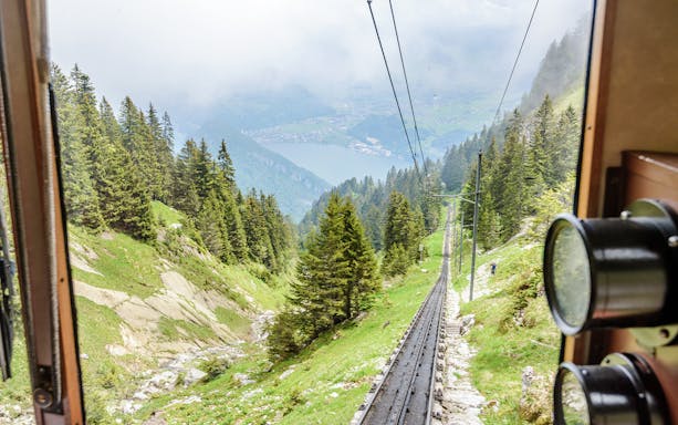 Mount Pilatus cogwheel train ascending through Swiss Alps with lake view.