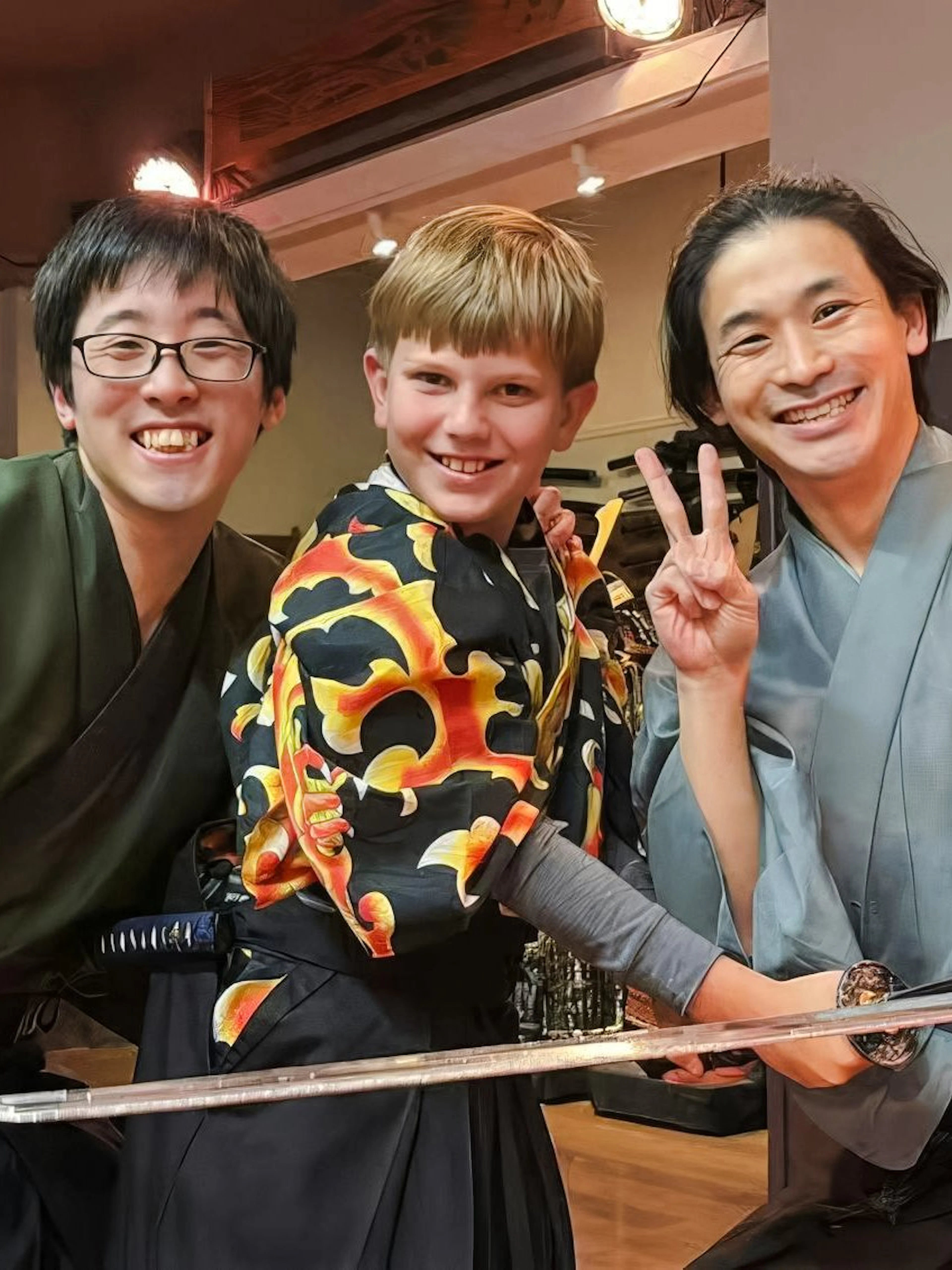 Kid posing with a sword at Samurai Experience with two instructors in traditional attire.