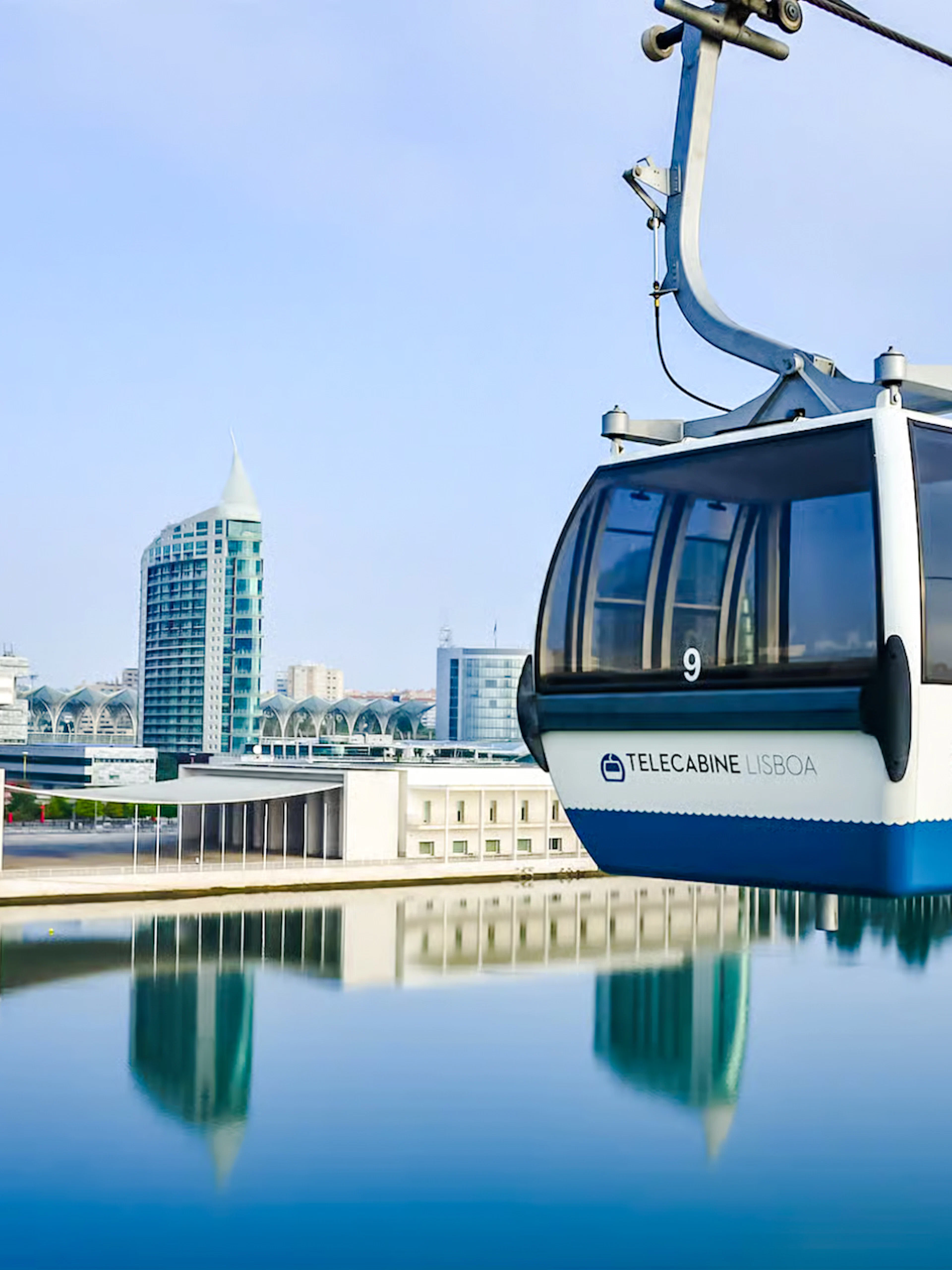 Lisbon cable car over water with cityscape in background.