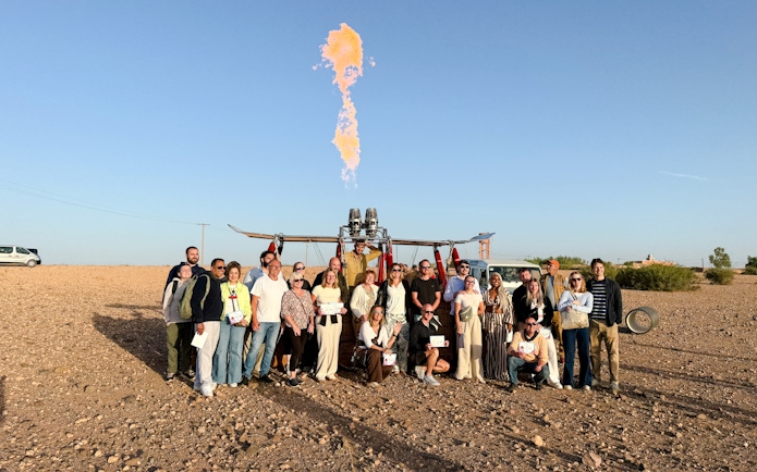 Group posing with hot air balloon in Marrakech desert.