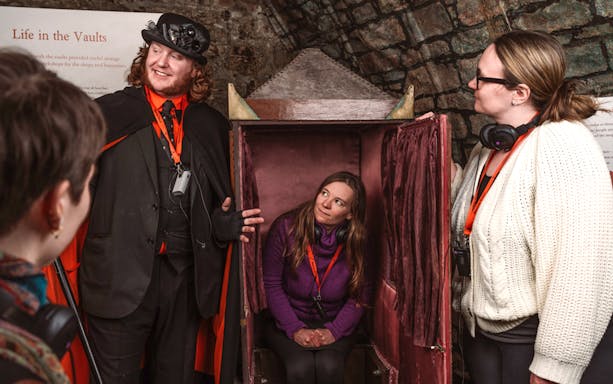 Tour guide in costume with visitors inside Edinburgh vaults during Ghostly Underground tour.