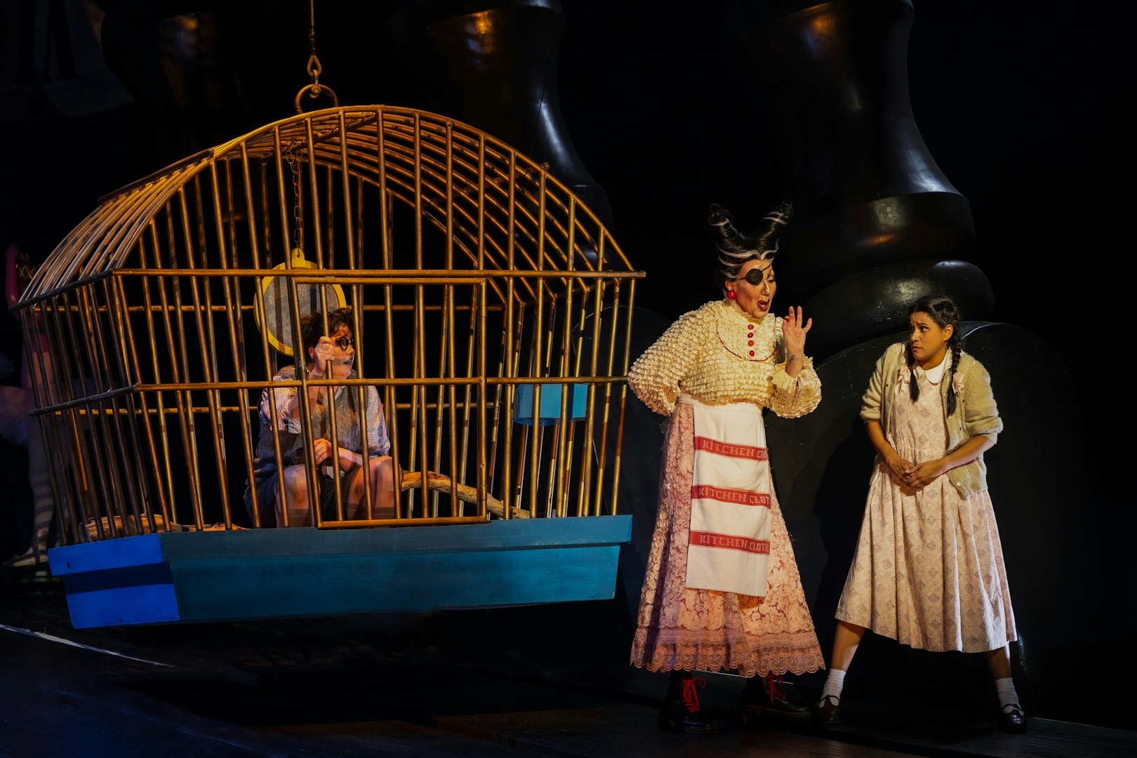 Hansel in a cage and Gretel with a witch during a stage performance of Hansel and Gretel.
