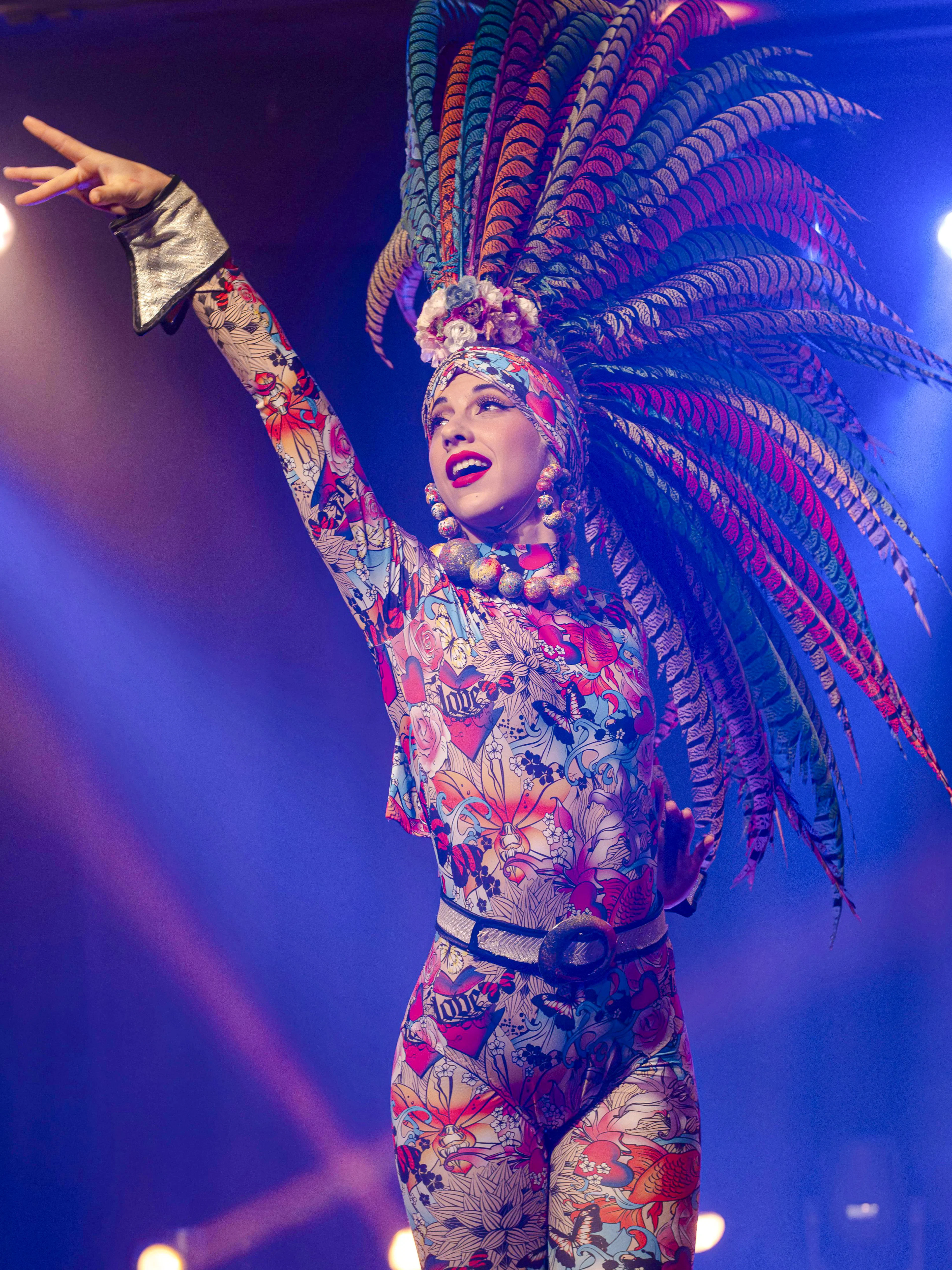 Performers in vibrant costumes with feathered headdresses at Les Nuits de Lola Oh Cesar, France.