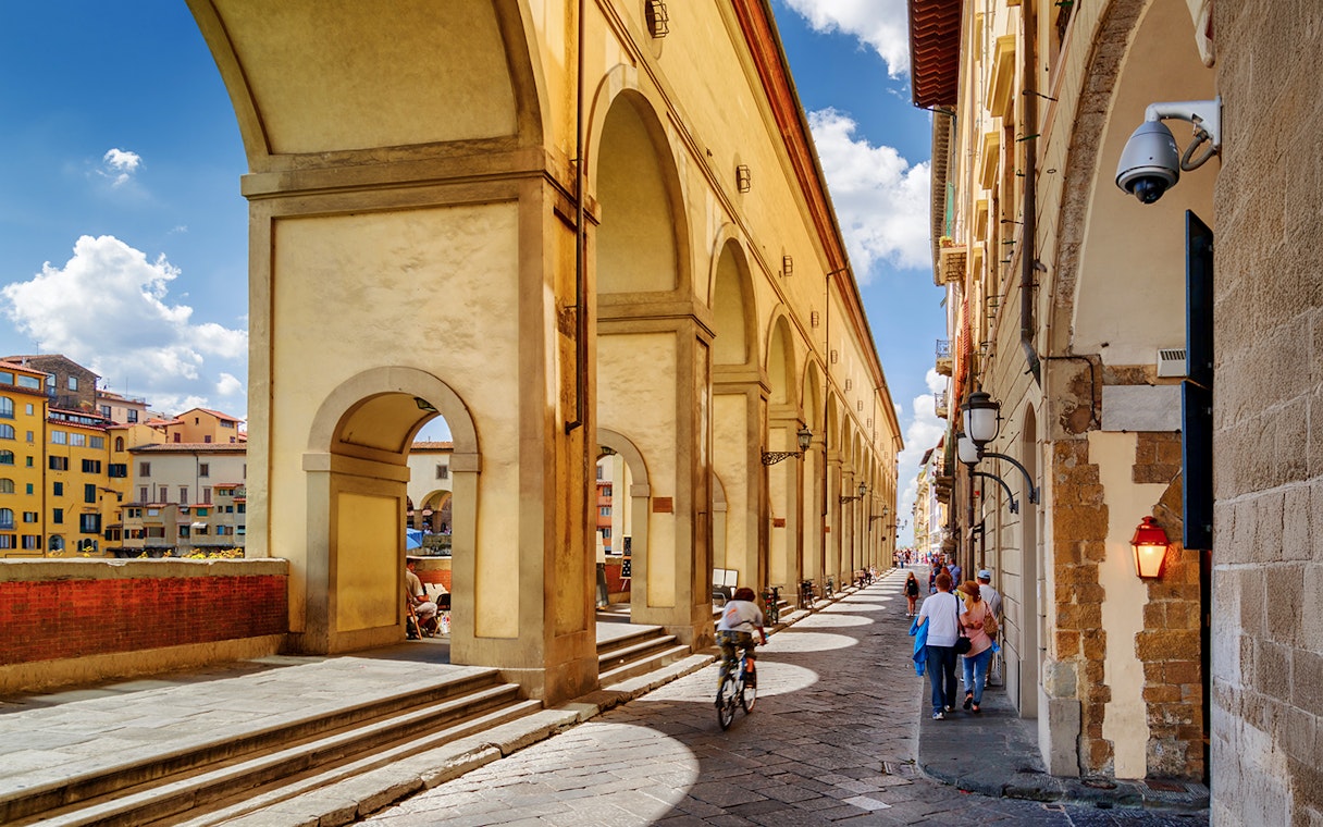 Vasari Corridor in Florence with people walking and cycling along the historic passage.