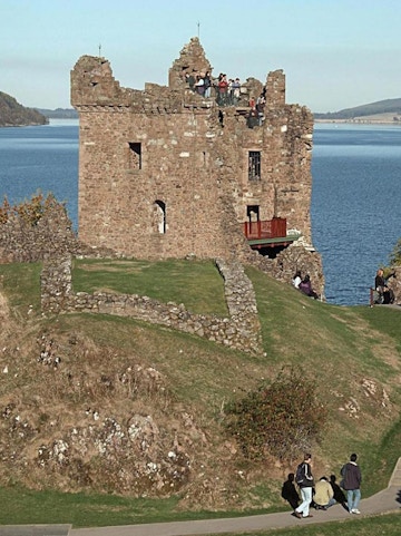 Urquhart Castle overlooking Loch Ness with visitors exploring the ruins.