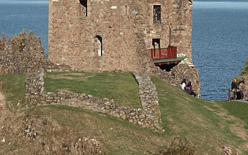 Urquhart Castle overlooking Loch Ness with visitors exploring the ruins.