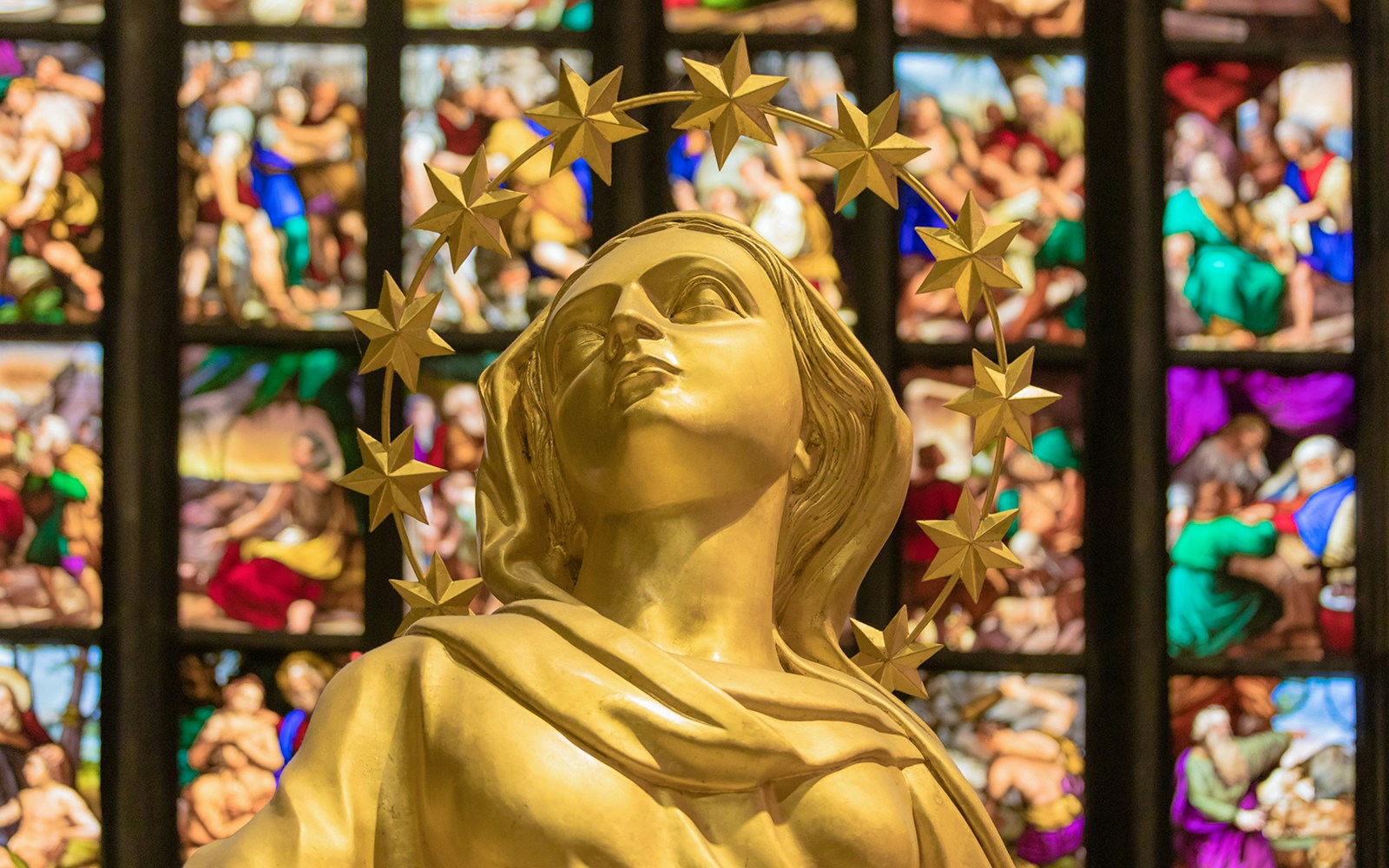 Golden statue inside Milan Duomo Cathedral with stained glass backdrop.