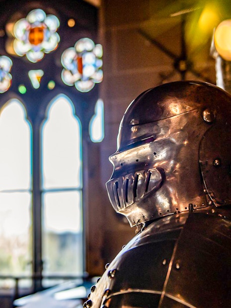Knight's armor inside Warwick Castle with stained glass window in the background.