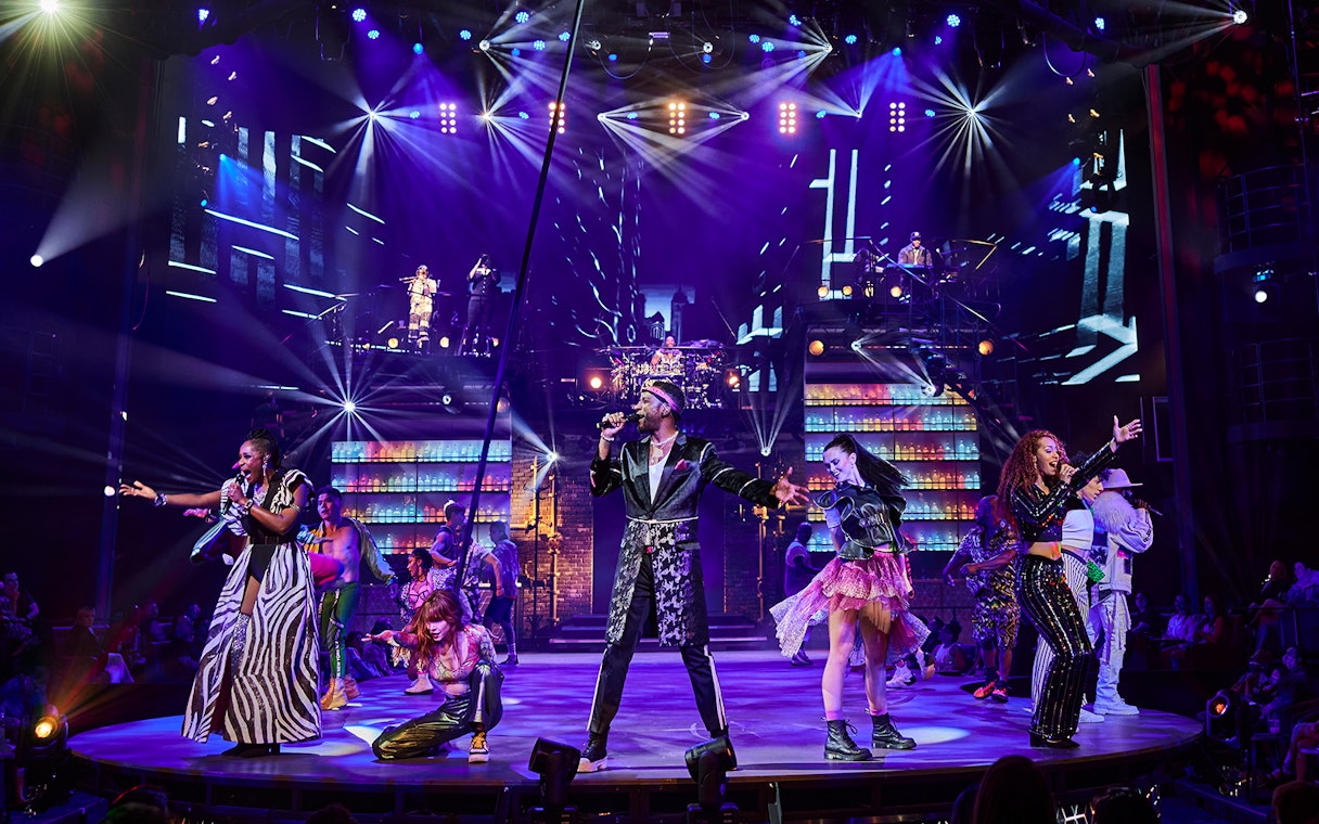 Performers on stage during the Mad Apple show with vibrant lights and costumes.