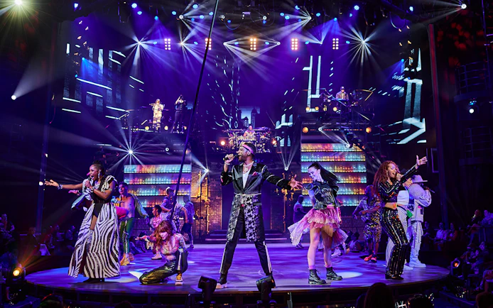 Performers on stage during the Mad Apple show with vibrant lights and costumes.