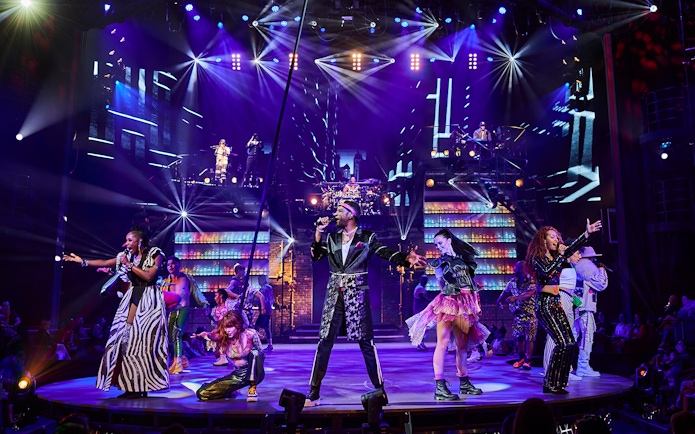 Performers on stage during the Mad Apple show with vibrant lights and costumes.