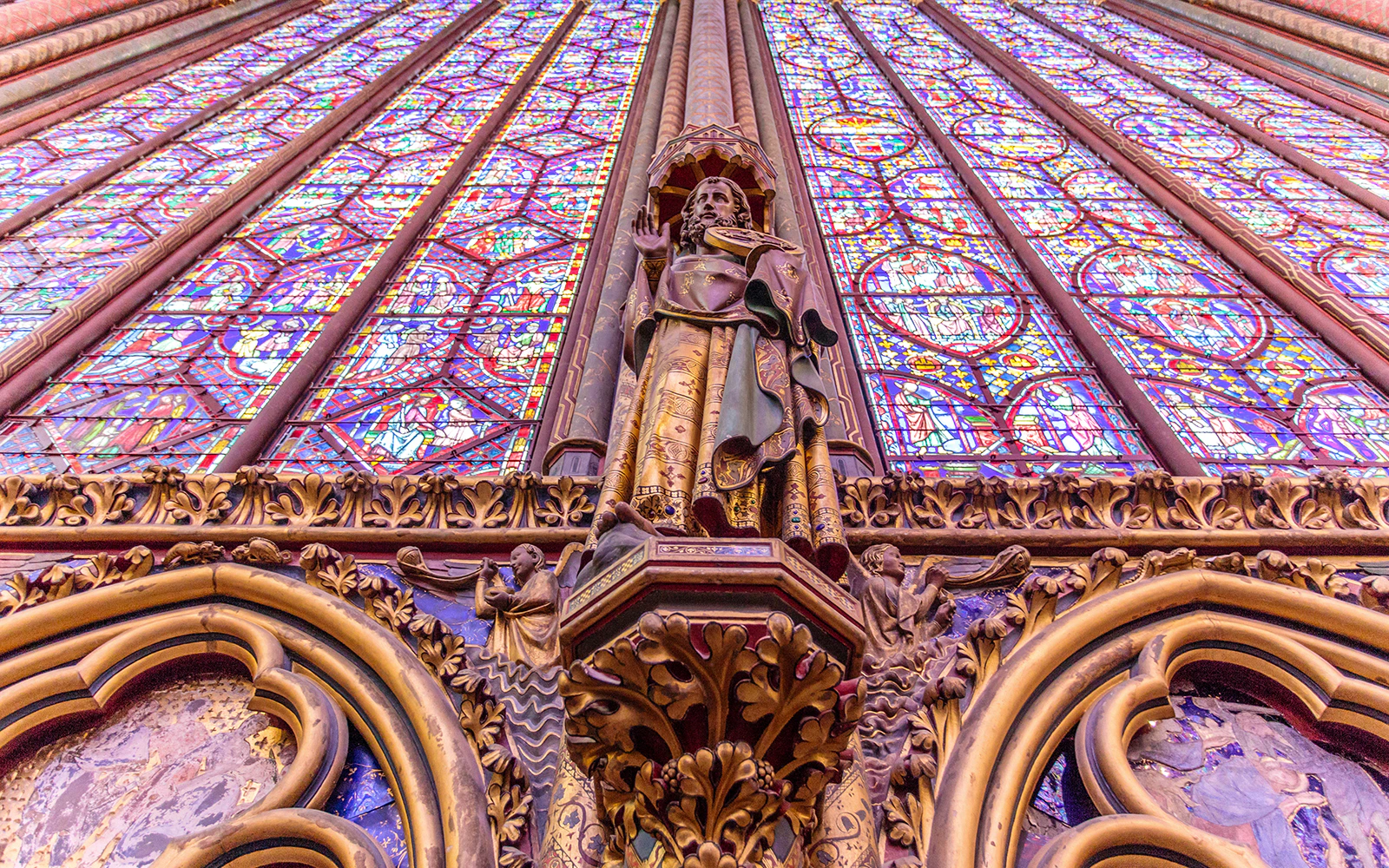 Statue of an Apostle on the north wall of Sainte-Chapelle, Paris, with stained glass backdrop.