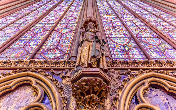 Statue of an Apostle on the north wall of Sainte-Chapelle, Paris, with stained glass backdrop.