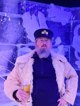 Man in captain's hat holding a beer at Berlin Icebar with ice sculptures in the background.