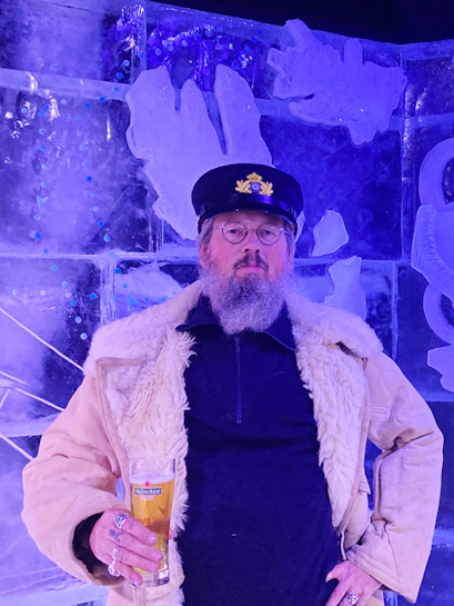 Man in captain's hat holding a beer at Berlin Icebar with ice sculptures in the background.