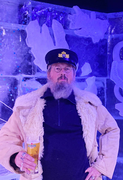 Man in captain's hat holding a beer at Berlin Icebar with ice sculptures in the background.