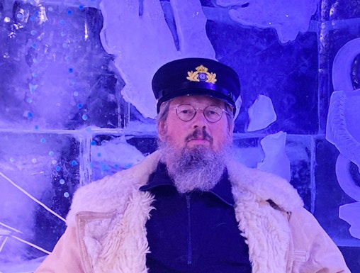 Man in captain's hat holding a beer at Berlin Icebar with ice sculptures in the background.