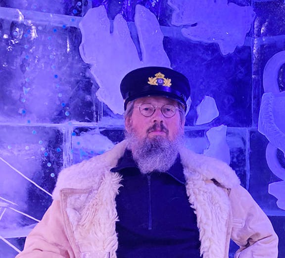 Man in captain's hat holding a beer at Berlin Icebar with ice sculptures in the background.