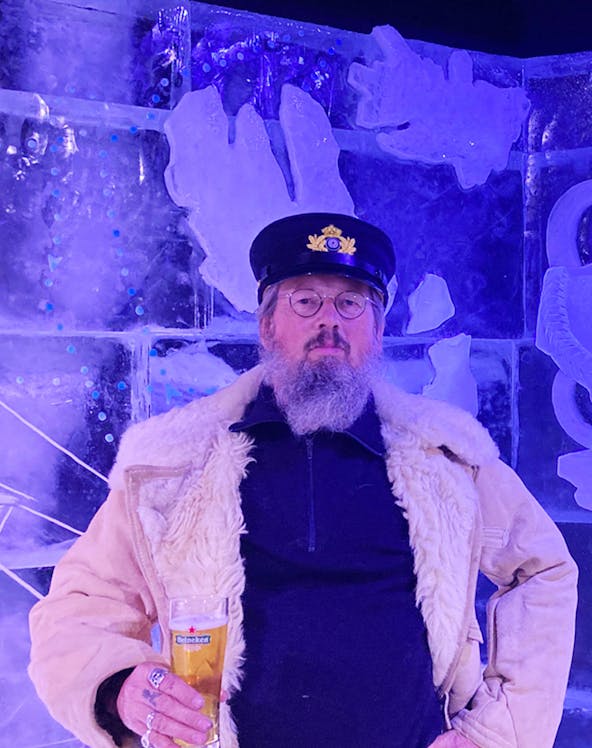 Man in captain's hat holding a beer at Berlin Icebar with ice sculptures in the background.