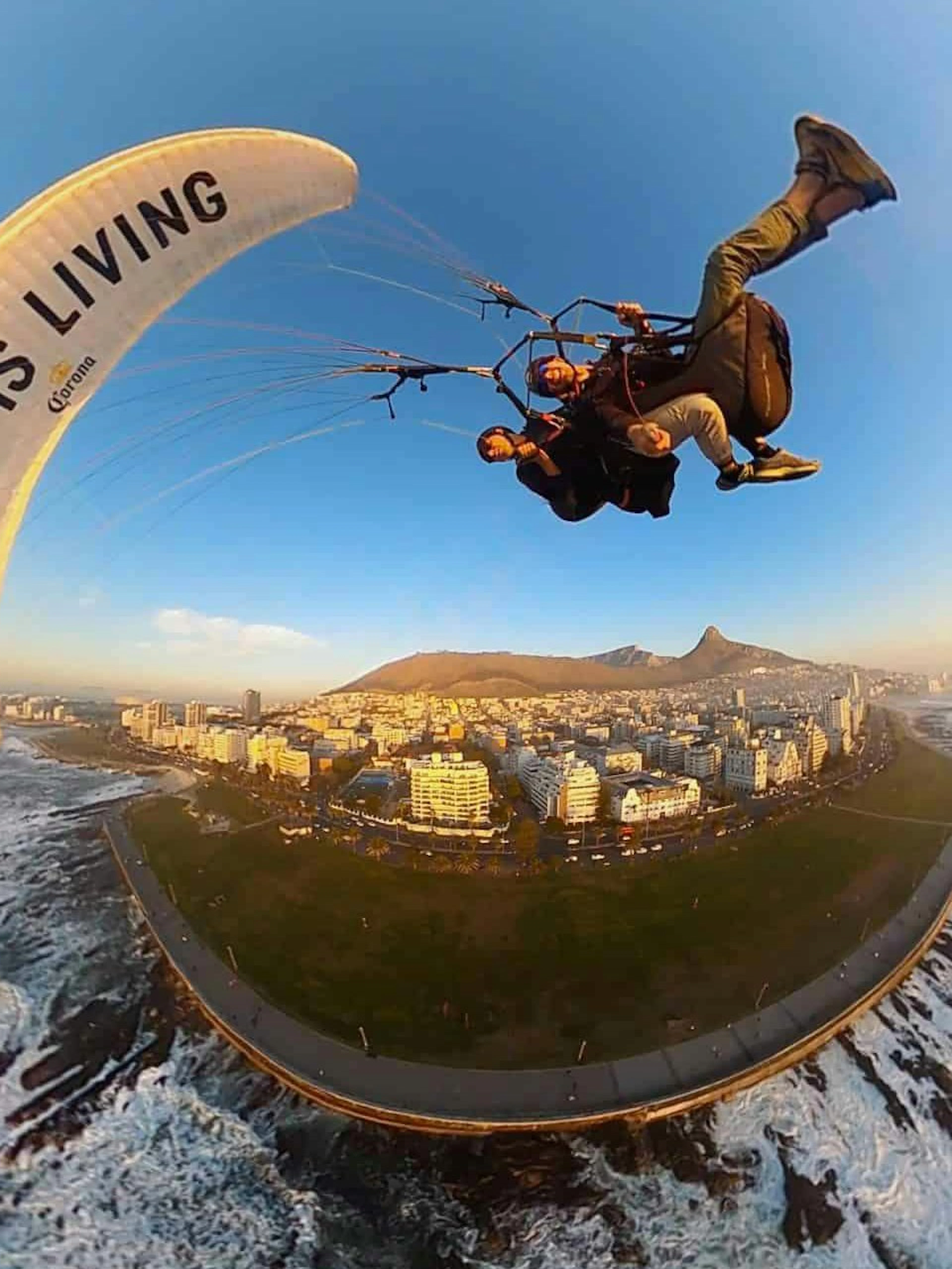 Tandem paragliding over Cape Town coastline with city and mountains in view.