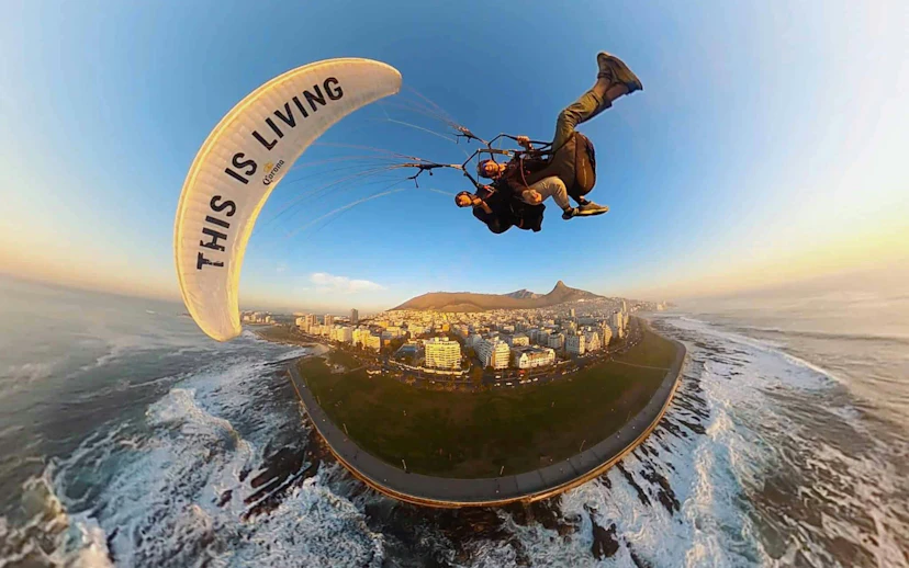 Tandem paragliding over Cape Town coastline with city and mountains in view.