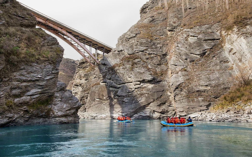 Rafting on Kawarau River with bridge and rocky cliffs in background.