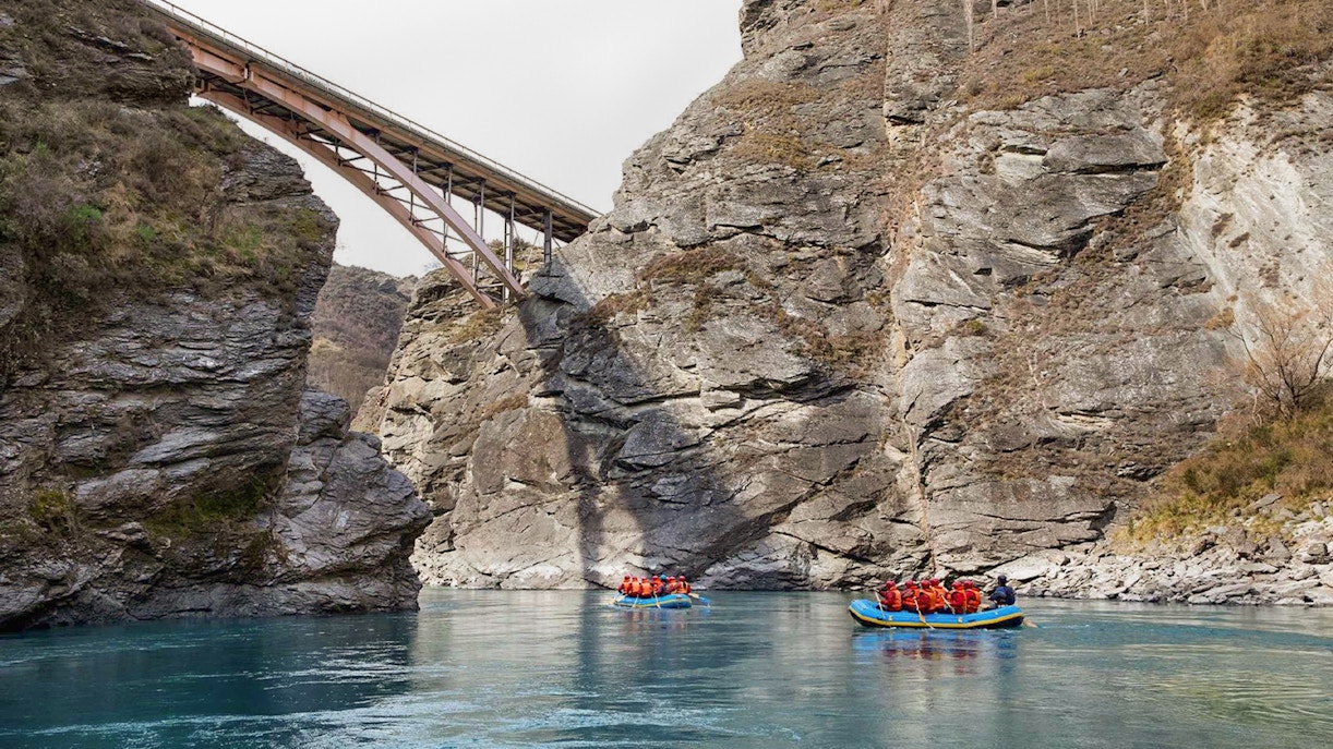 Rafting on Kawarau River with bridge and rocky cliffs in background.
